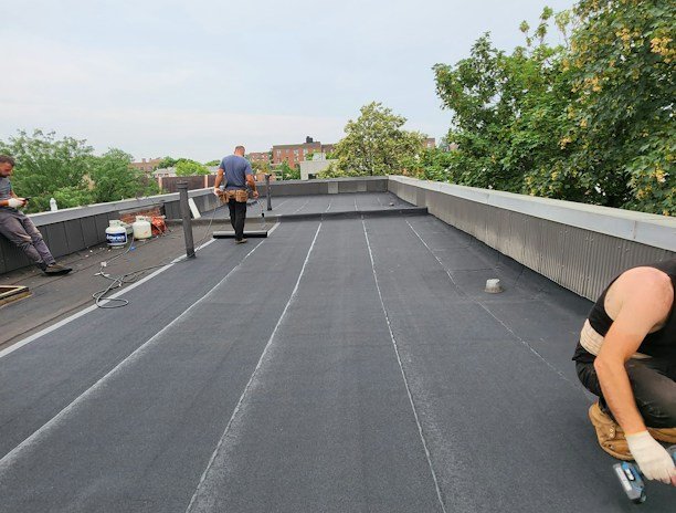 Construction workers applying waterproofing materials on a commercial building site.
